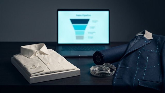 Folded off-the-rack shirt next to a tailored jacket with chalk marks and a measuring tape, a sales pipeline on a laptop behind