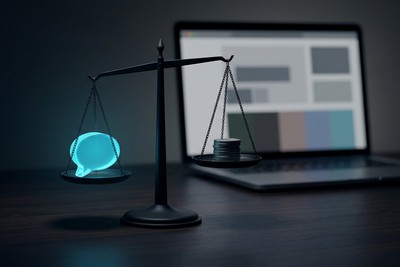 Balance scale weighing a glowing cyan chat bubble against a small stack of coins, with a laptop behind
