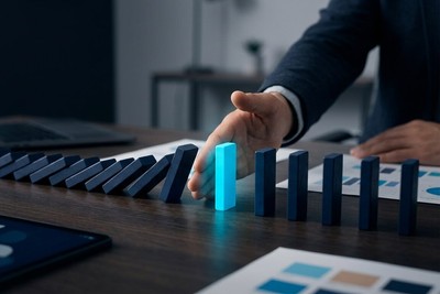 Hand placing a cyan domino to stop a falling chain of dark dominoes before it reaches the last ones