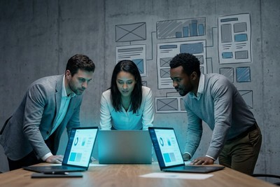 Three-person founding team leaning over laptops in front of a wall of wireframe sketches