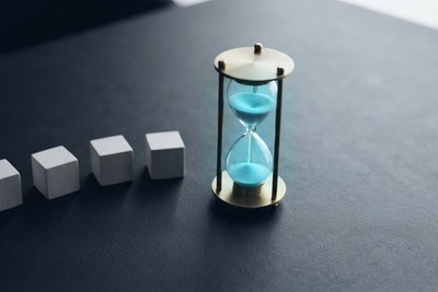 Hourglass on a desk beside four small labeled blocks representing the variables that set a project's pace