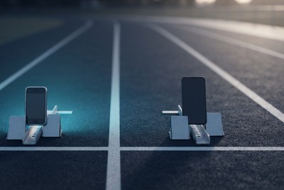 Two smartphones standing in starting blocks on a running track, one lit by cyan light, ready to race